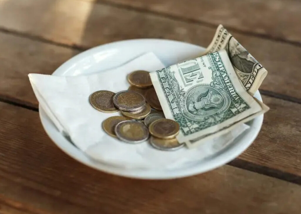 A familiar sight in American restaurants: a tip left on the table. In the U.S., this “optional” extra is anything but optional – it’s a crucial part of workers’ income. In many other countries, however, leaving extra coins or bills would be unusual or even unwelcome. Changing how we think about that little dish of cash could transform the lives of millions of service workers. The Toxic Legacy of Tipping